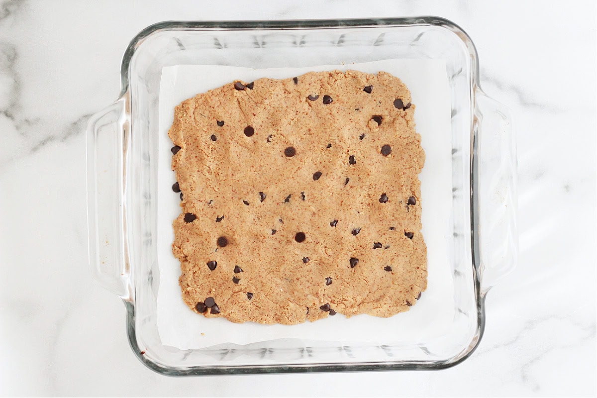 Cookie dough bark pressed flat on a piece of parchment paper in an 8x8 pan.