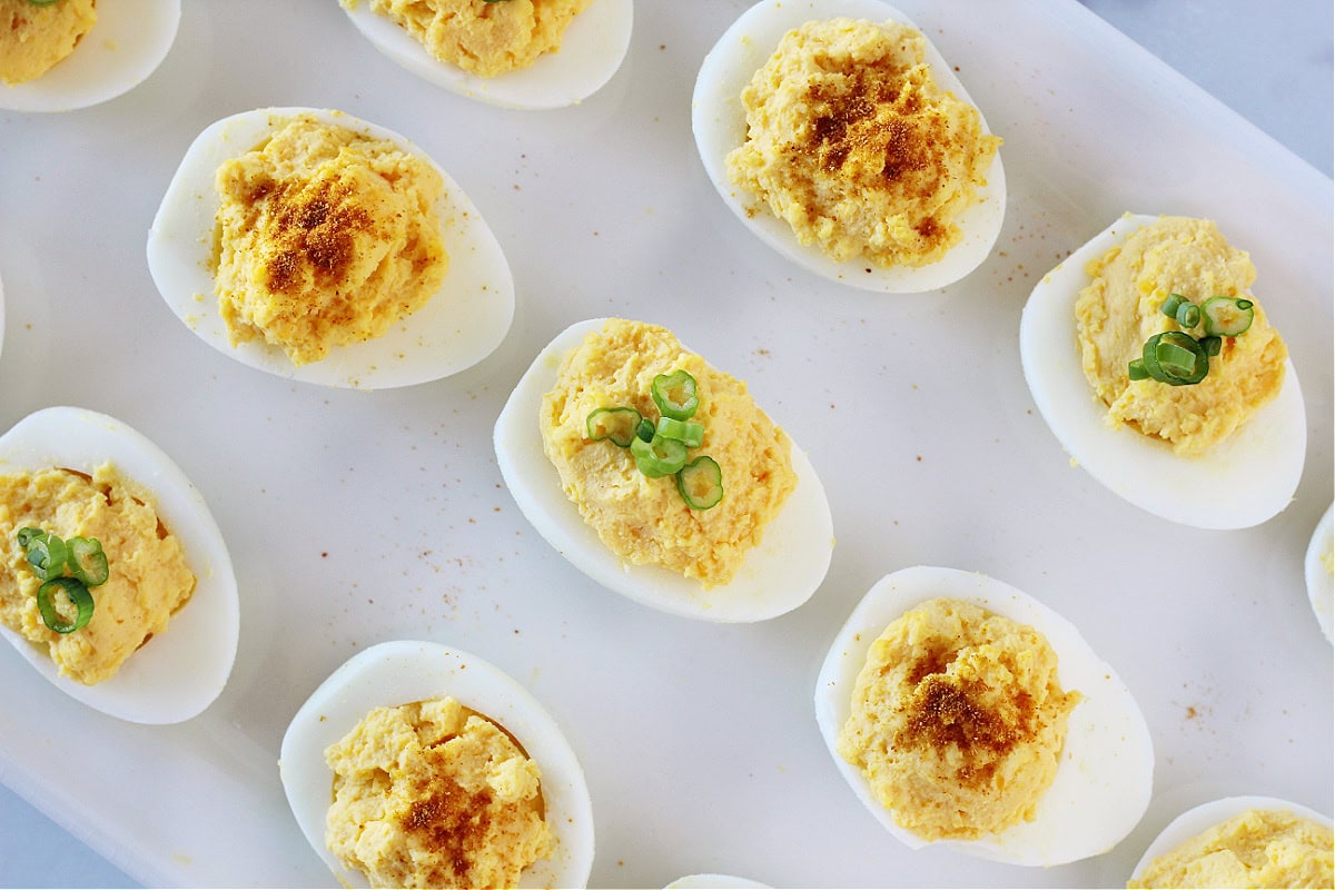 Deviled eggs on a white platter topped with paprika or sliced green onions.