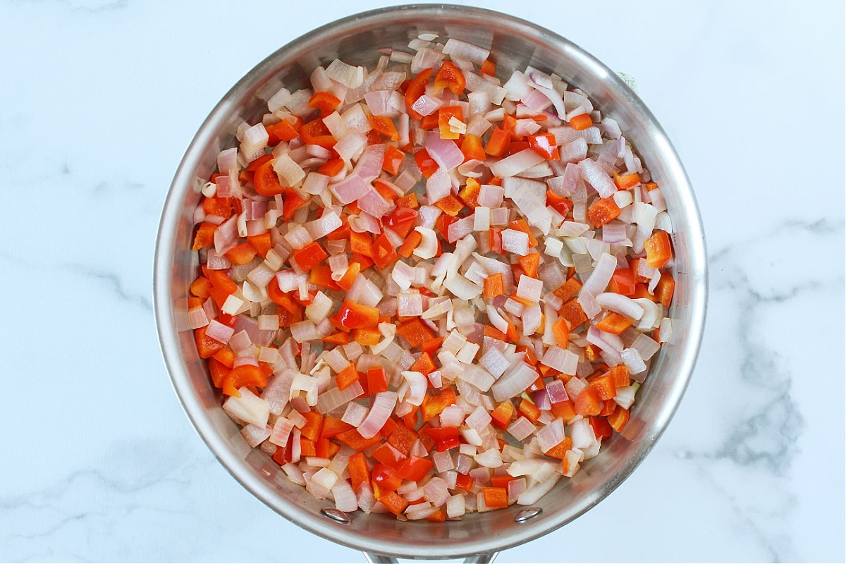 Sauteed red onion and red bell pepper in a sauté pan.