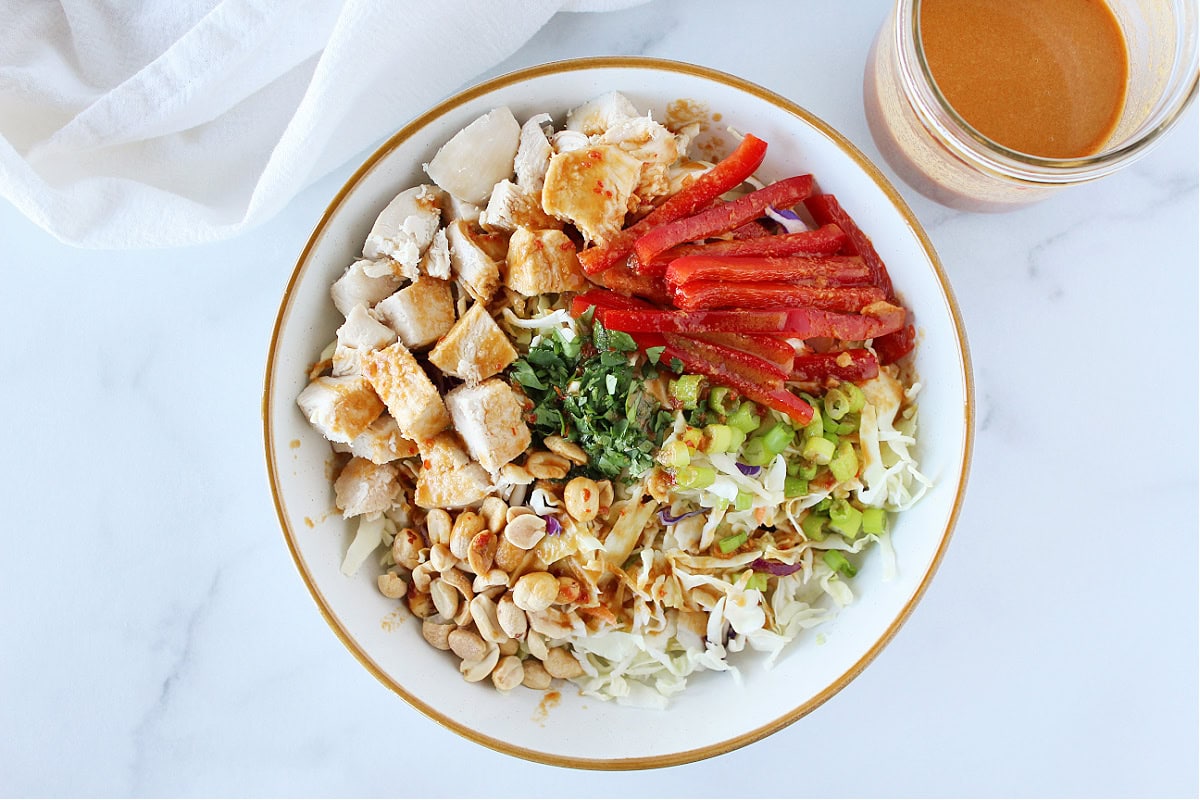 A creamy peanut dressing poured over chicken coleslaw salad in a white bowl.