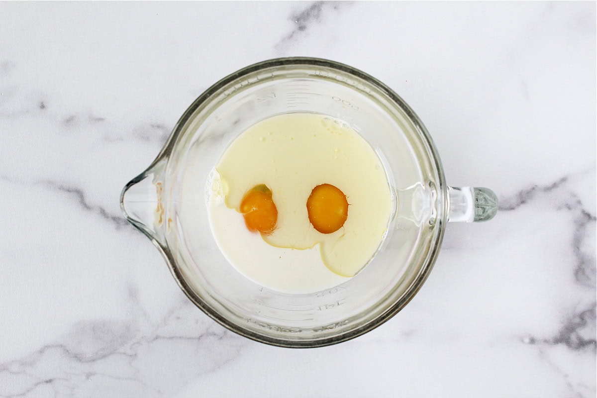 Two eggs, oil, and milk in a glass mixing bowl.