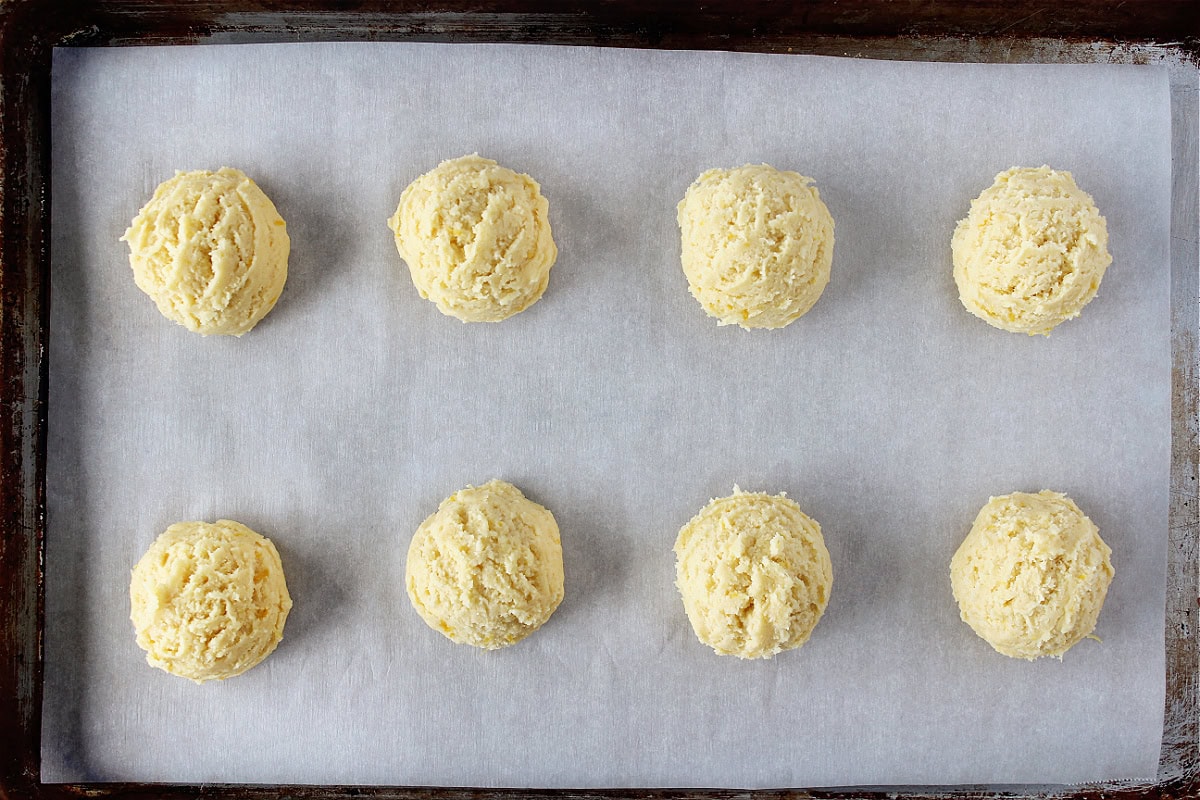 Eight cookie dough balls on parchment paper on a baking sheet.