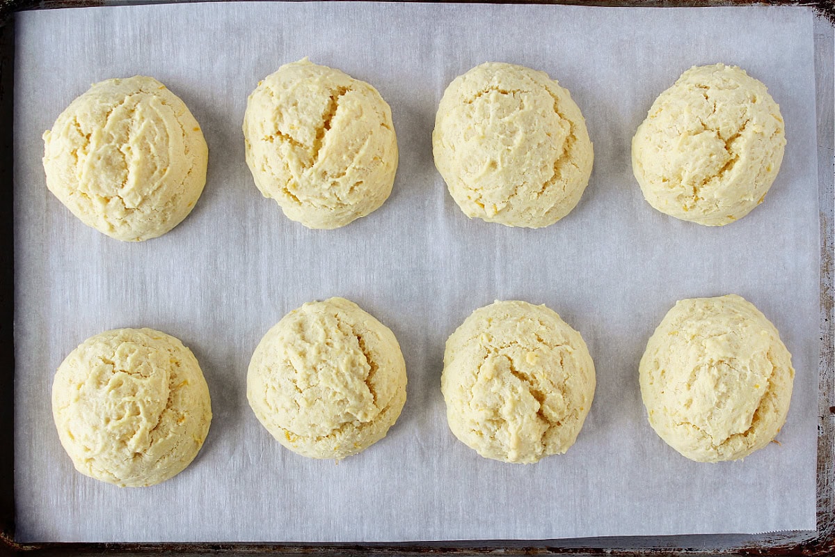 Eight fluffy lemon cookies on a baking sheet lined with parchment paper.