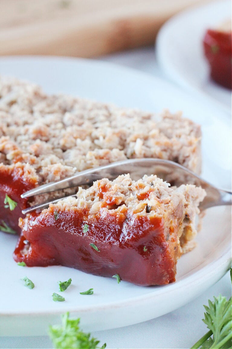 A fork cutting into a slice of meatloaf on a white plate.