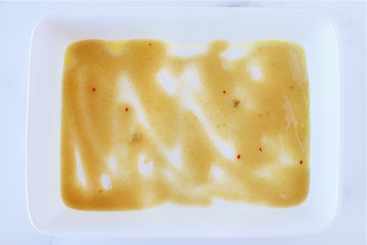 Green enchilada sauce on spread thinly on the bottom of a white baking dish.