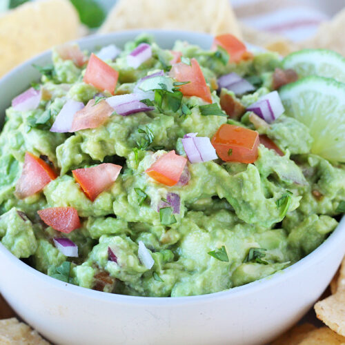 Guacamole topped with fresh red onion, tomatoes, cilantro a two lime slices.
