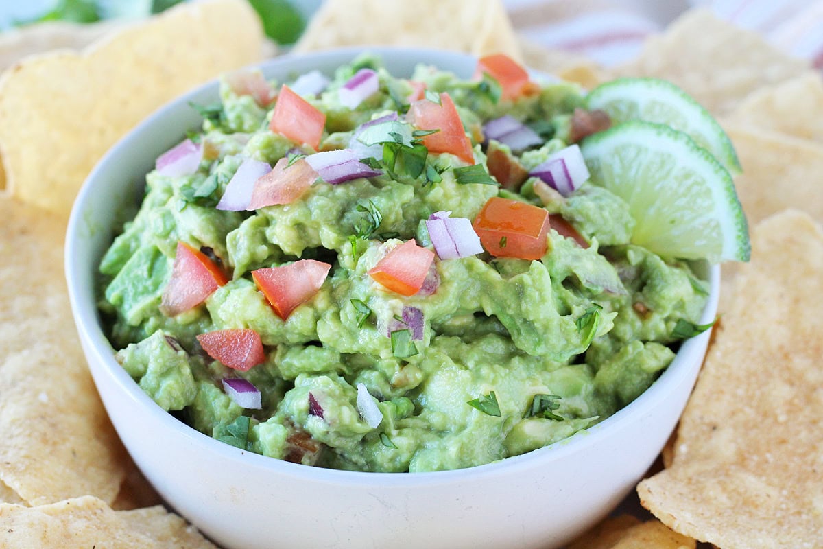 Guacamole topped with fresh red onion, tomatoes, cilantro a two lime slices.