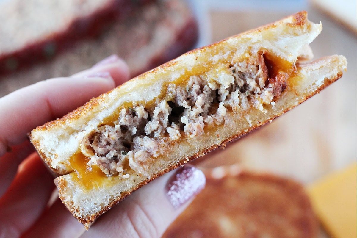 A woman's hand holding a grilled cheese burger sandwich cut in half.