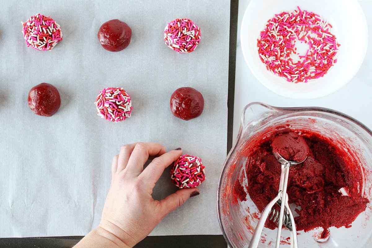 Using a cookie dough scoop to make cookies, some rolled in sprinkles.