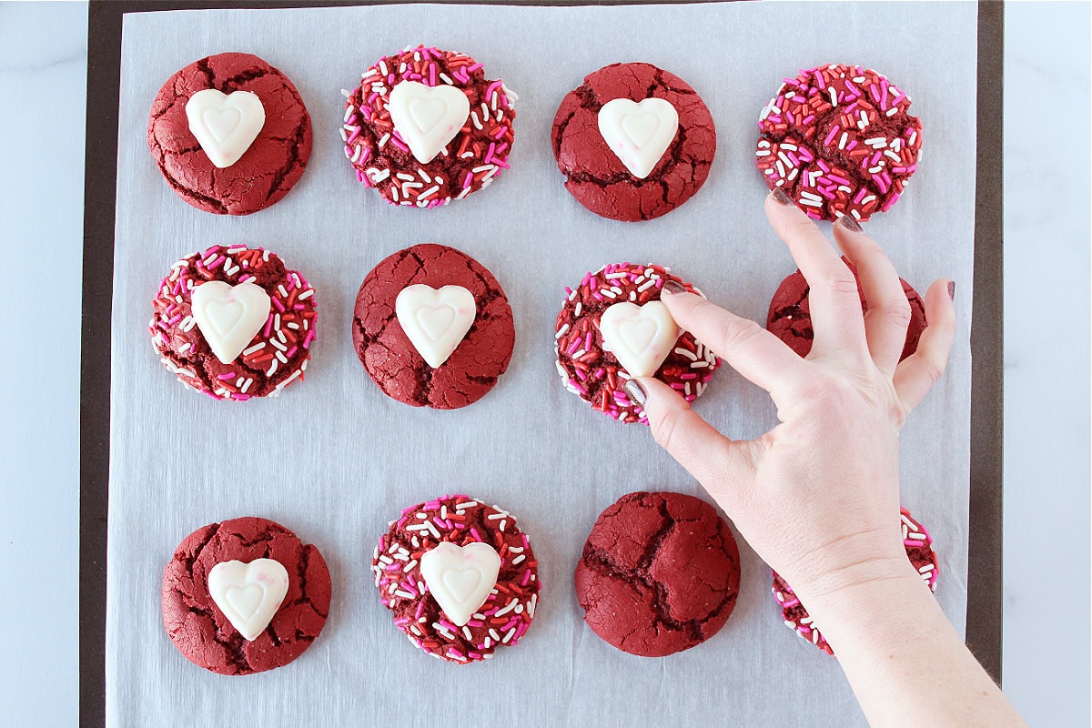 Placing white chocolate hearts on top of red velvet cookies.