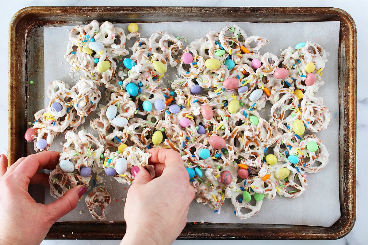 A woman's hands breaking apart Easter candy pretzel bark on a baking sheet.