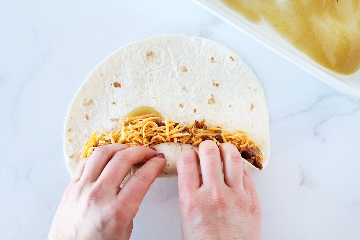 A woman's hands rolling up a tortilla with ground beef filling and shredded cheese.