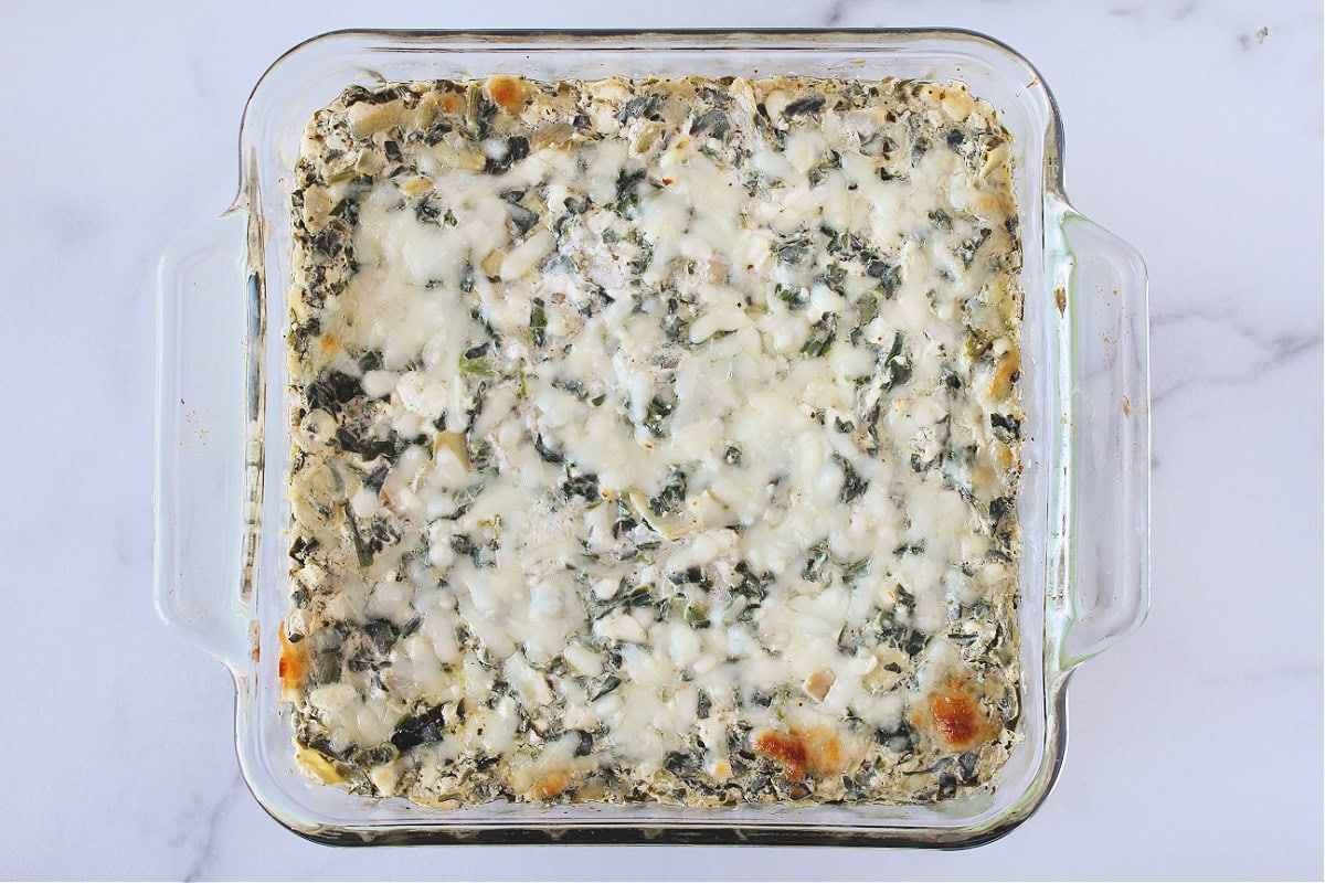 A pan of baked spinach artichoke dip with melted mozzarella cheese on top.