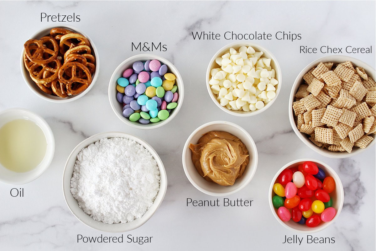 Bowls of oil, pretzels, powdered sugar, pastel M&Ms, white chocolate chips, peanut butter, jelly beans, and Rice Chex cereal.