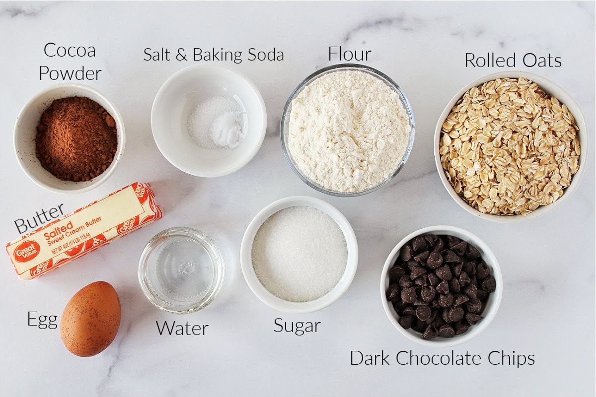 Labeled ingredients for double chocolate oatmeal cookies on a white marble countertop.