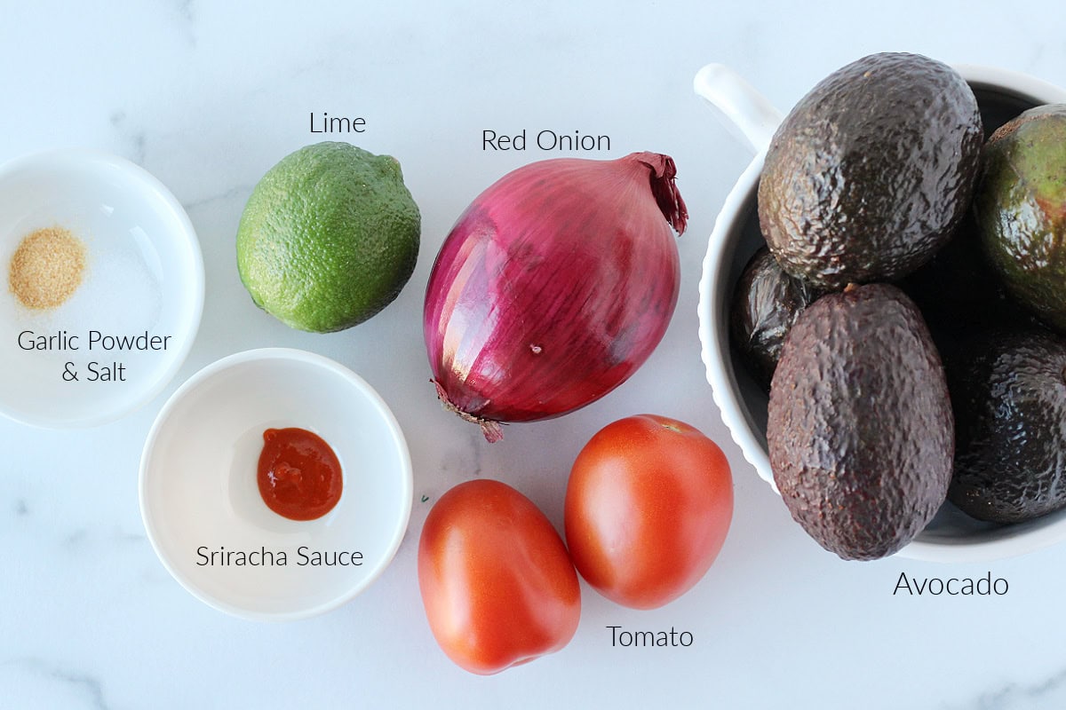 Labeled ingredients for homemade guacamole on a white marble countertop.