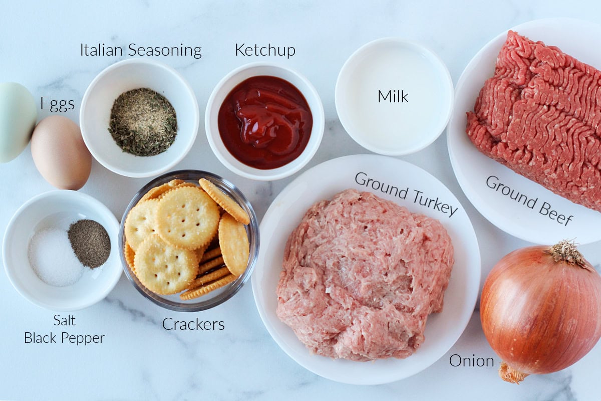 Labeled ingredients for homemade meatloaf on a white marble cutting board.