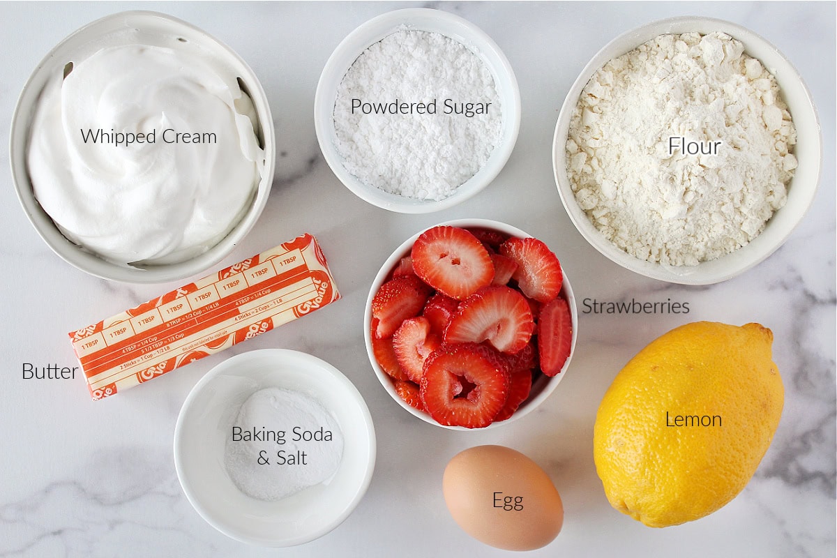 Labeled ingredients for lemon strawberry shortcake on a white marble countertop.