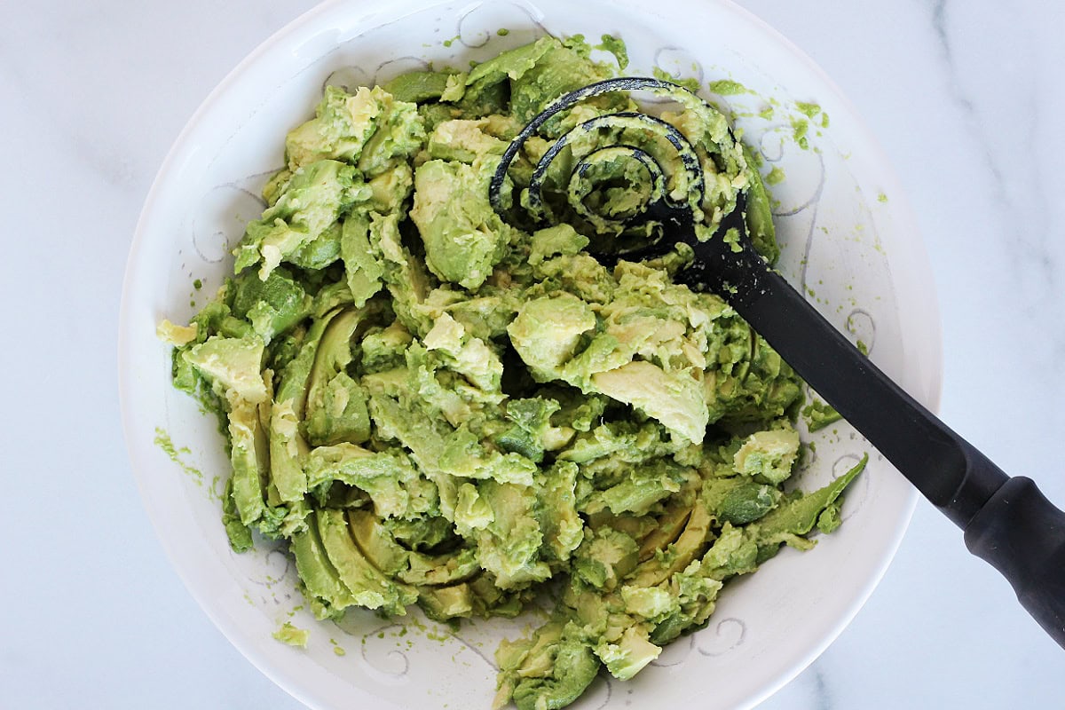 Mashing avocados in a white bowl with a silicone avocado masher.