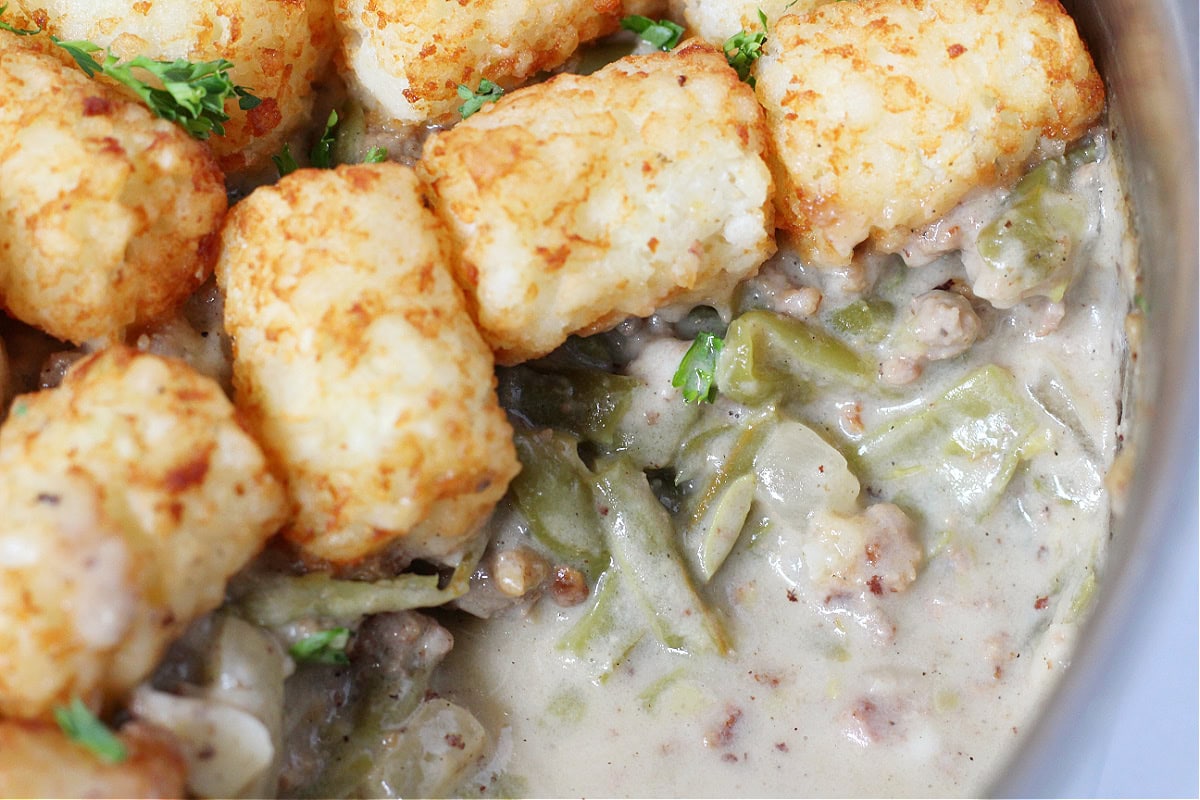 Tater tots on top of a creamy meat and green bean mixture.