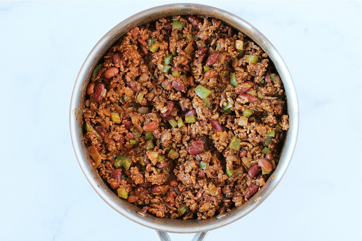 Browned ground beef with veggies and chili beans sectioned in a sauté pan.