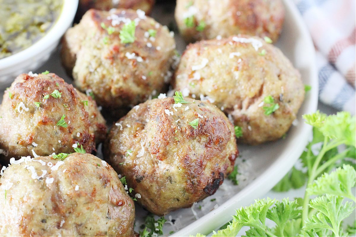 Air fryer turkey pesto meatballs topped with chopped parsley and shredded parmesan.