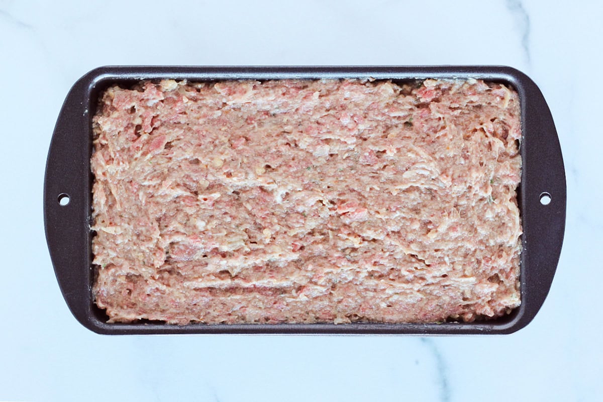 Meatloaf batter pressed into a metal meatloaf pan.