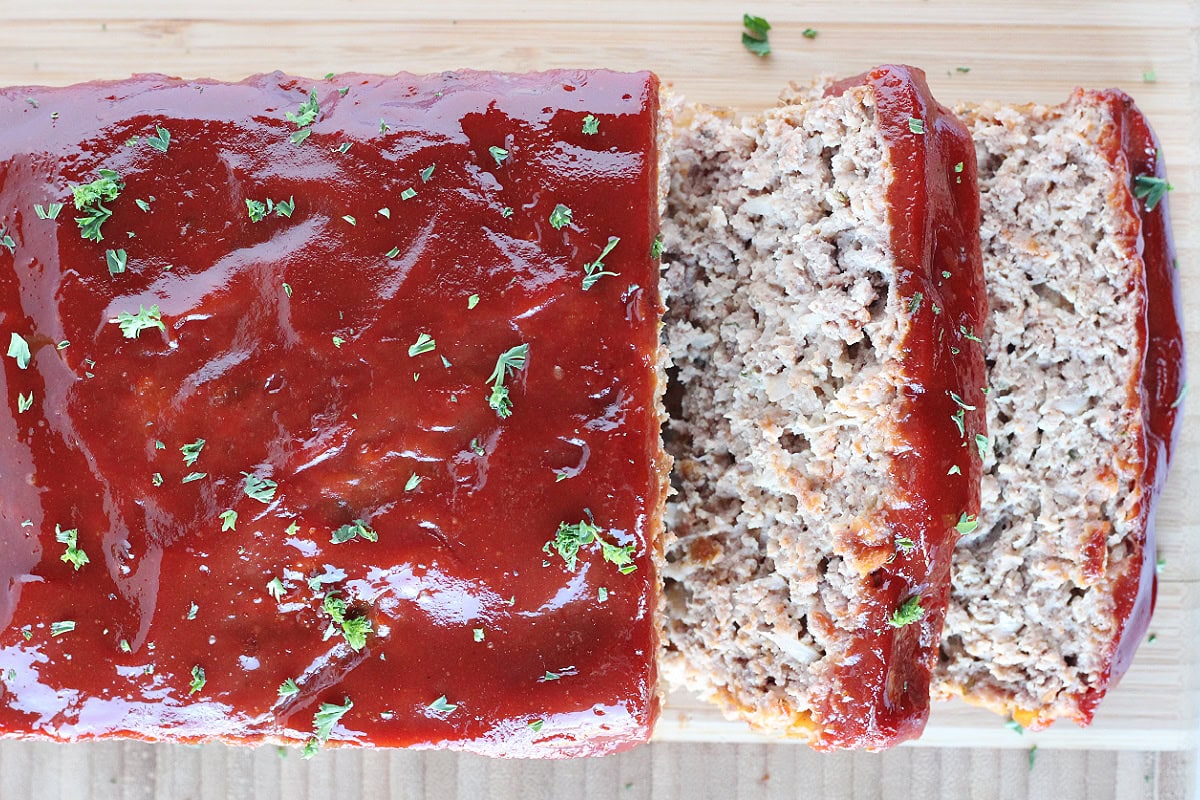 Two slices of meatloaf with the loaf on a wooden cutting board.