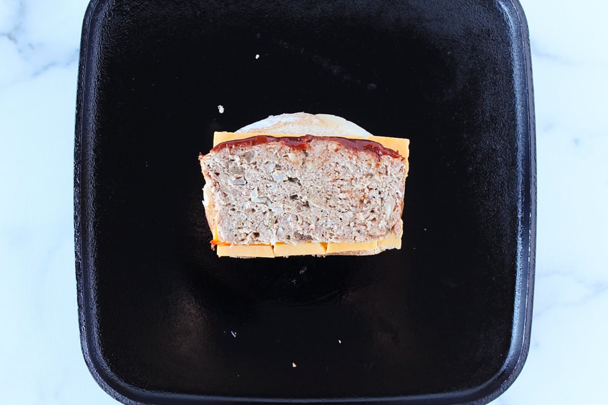 A slice of meatloaf on top of sliced cheese on a slice of bread.