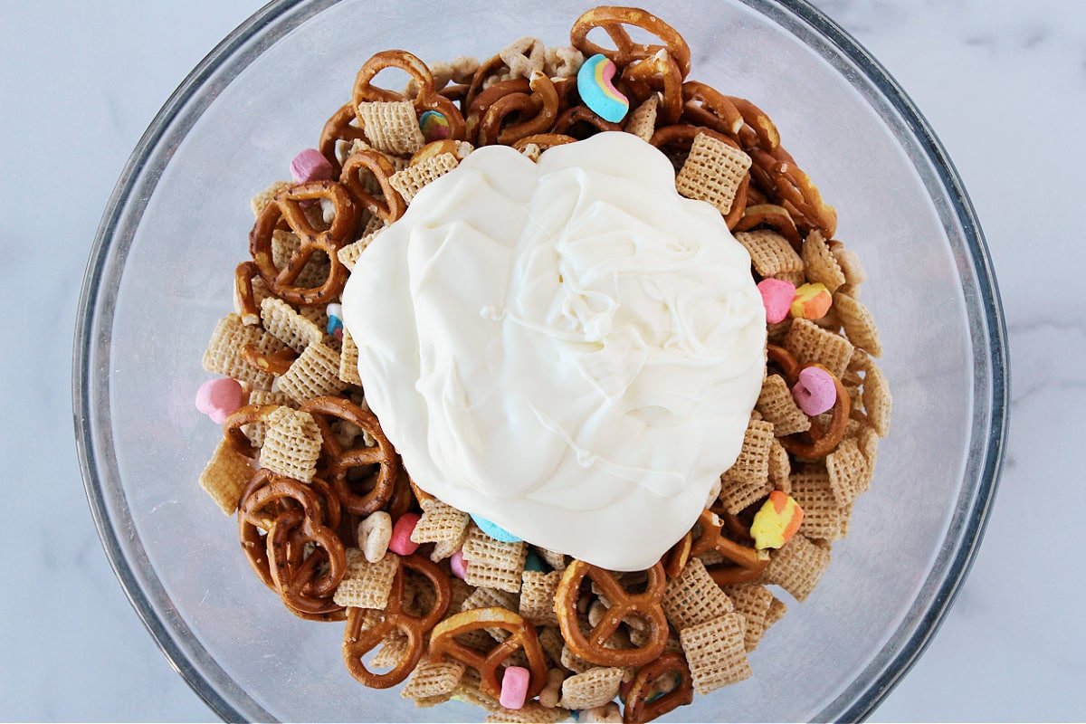 Melted white chocolate on top of Chex cereal, pretzels, and Lucky Charms marshmallows in a bowl.