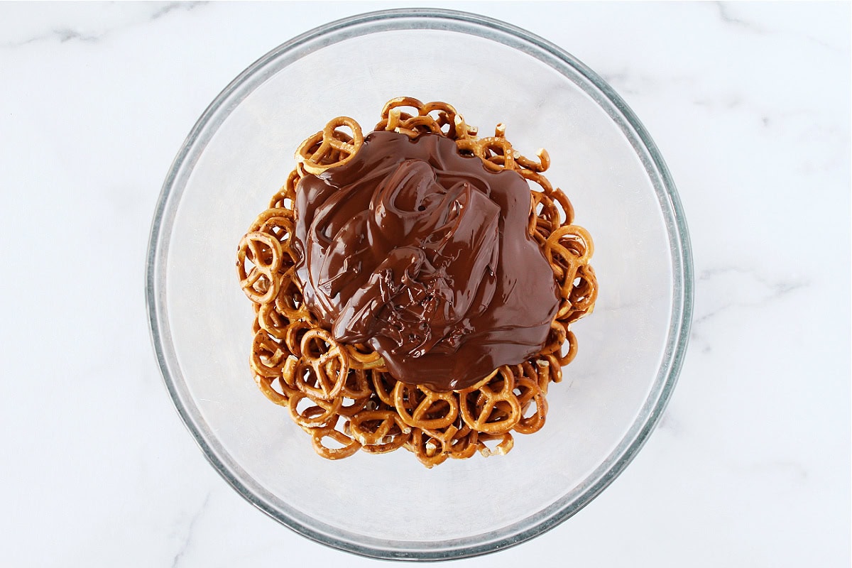 Melted chocolate over twisty pretzels in a glass bowl.