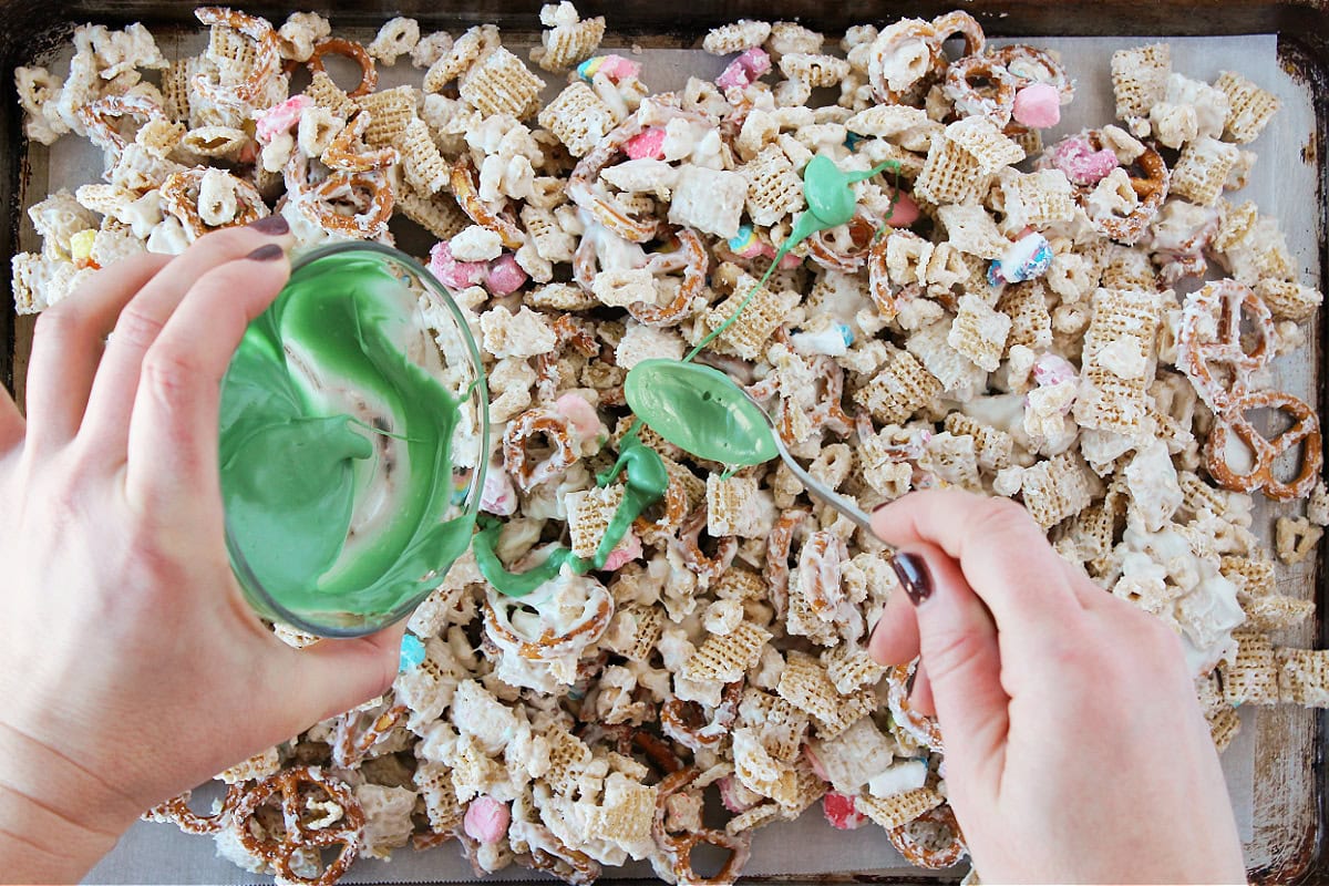 Two hands drizzling green white chocolate over leprechaun bait on a baking sheet.