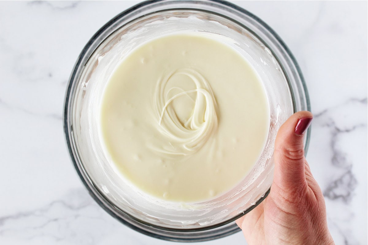 A woman's hand holding a bowl of melted white chocolate chips.