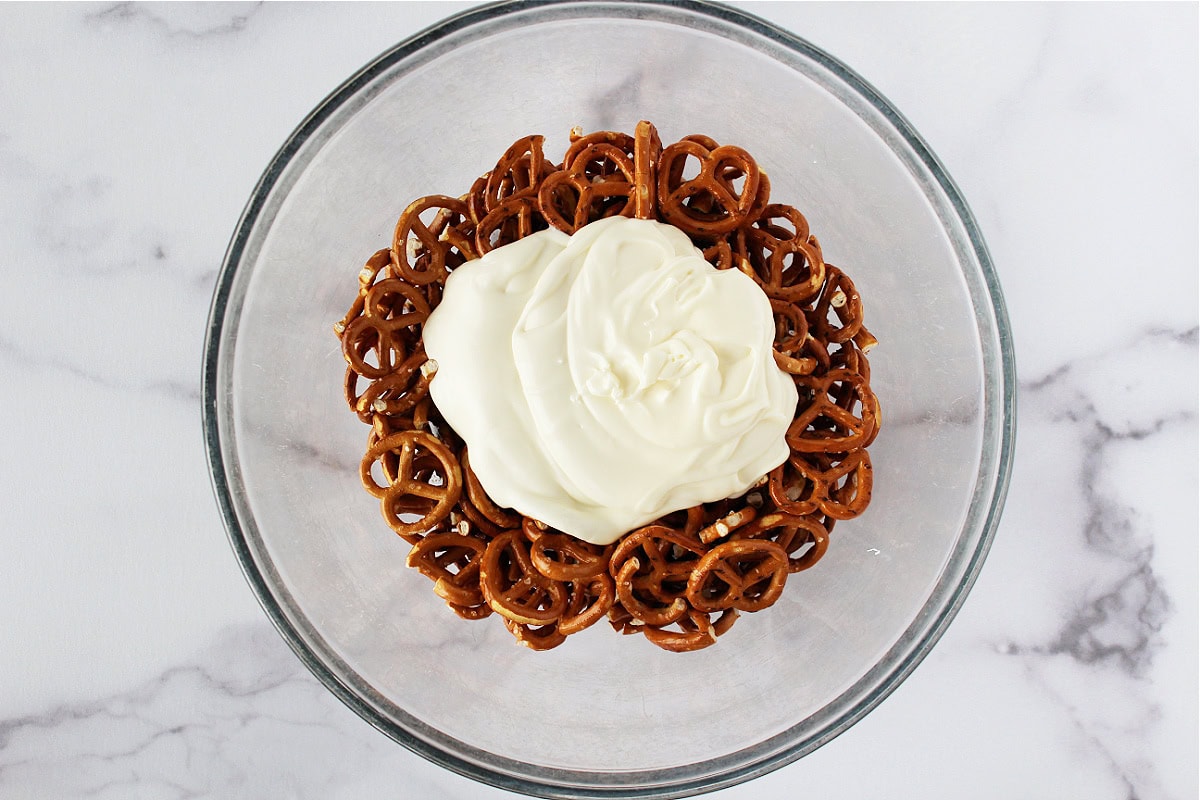 Melted white chocolate on top of twisty pretzels in a mixing bowl.