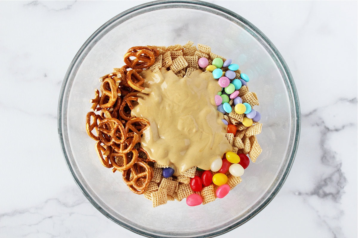 A bowl of pretzels, Chex cereal, pastel M&Ms, and jelly beans with a white chocolate peanut butter mixture on top.