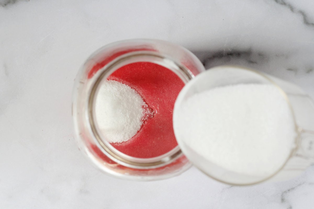 Pouring monk fruit sweetener into a jar of raspberry puree.