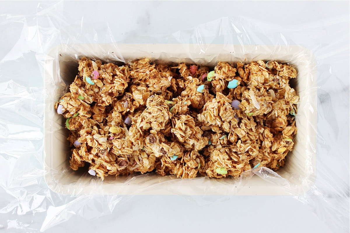 No bake oat bars batter sitting atop plastic wrap in a bread pan.