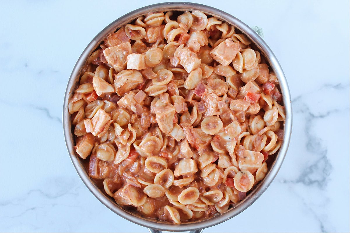Pasta, diced chicken breast and red bell pepper coated in rosa sauce in a large pan.