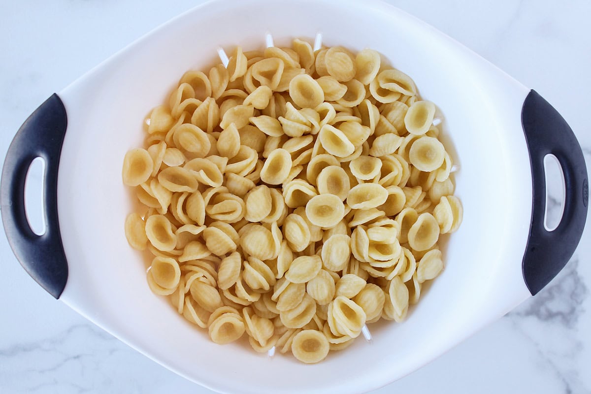Cooked orecchiette pasta in a white strainer.