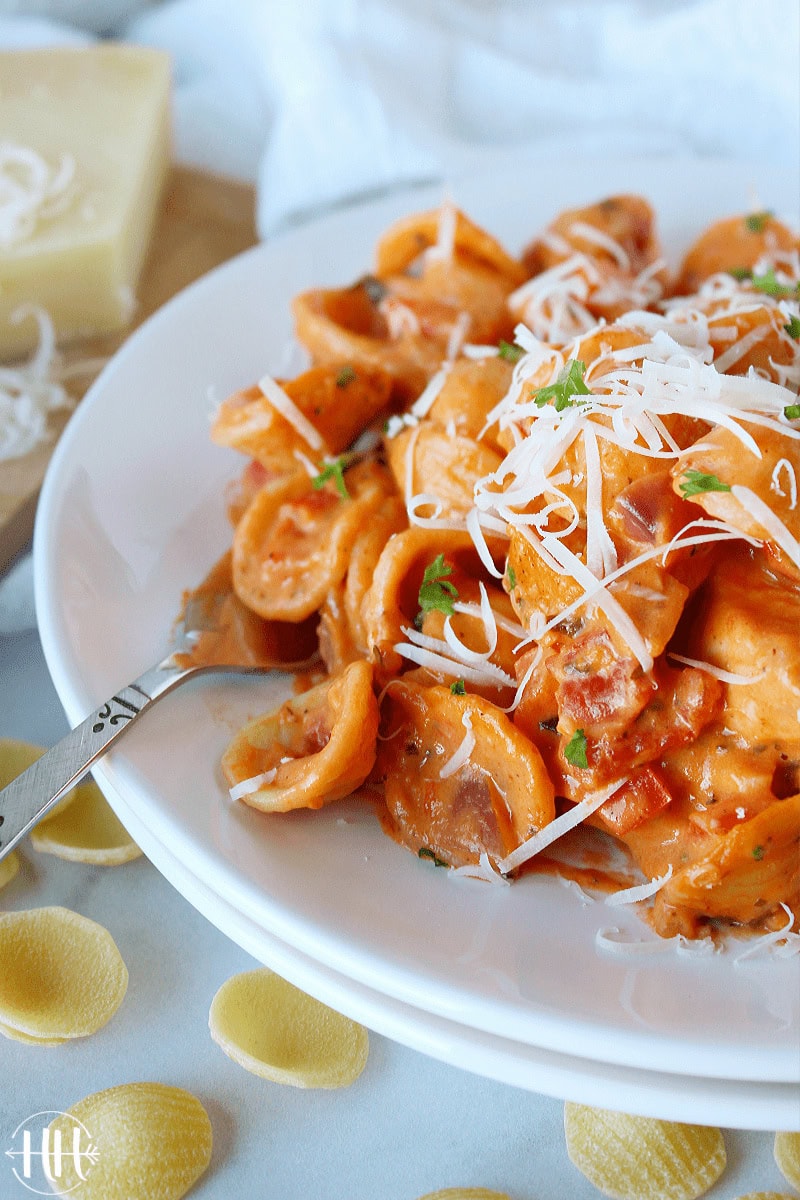A fork digging into chicken orecchiette in rosa sauce on a white plate.