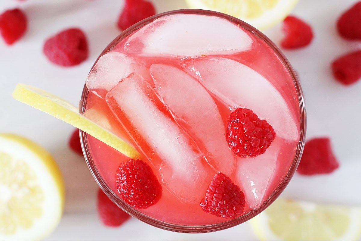 Ice cubes, fresh raspberries and a lemon slice in a glass of raspberry lemonade.