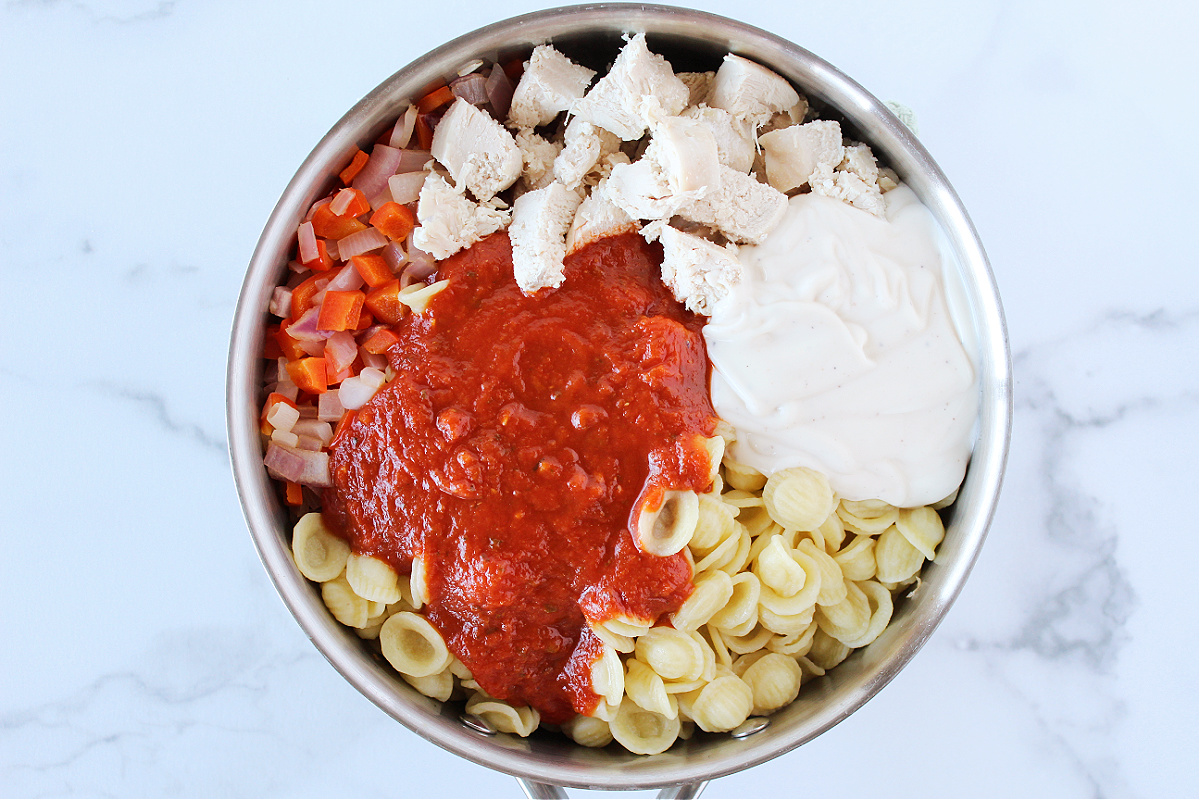 Marinara sauce, alfredo sauce, chicken, vegetables and pasta in a large sauté pan.