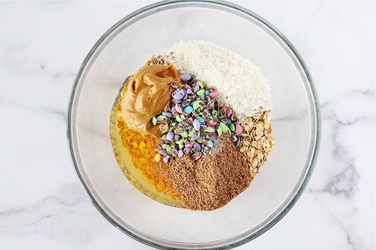Glass mixing bowl with peanut butter, shredded coconut, honey and crushed M&Ms.