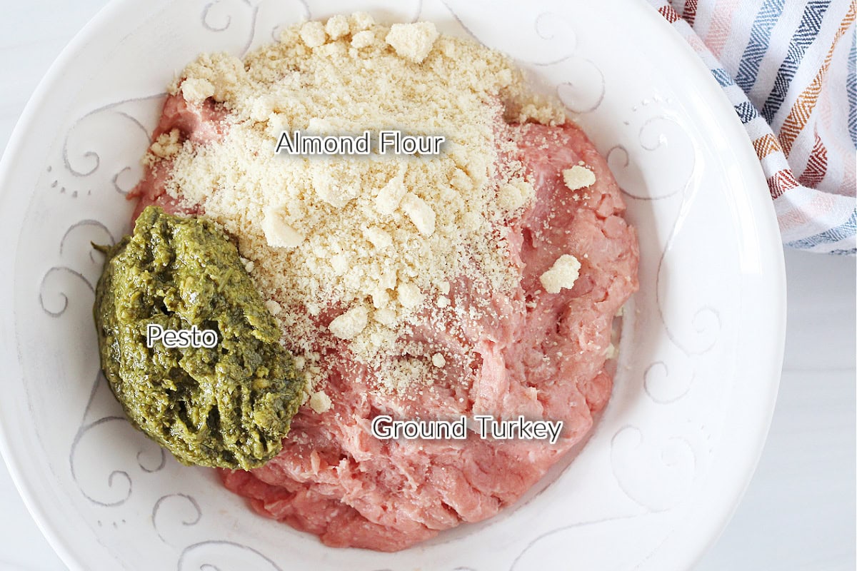 Labeled ingredients in a bowl for turkey pesto meatballs with almond flour.