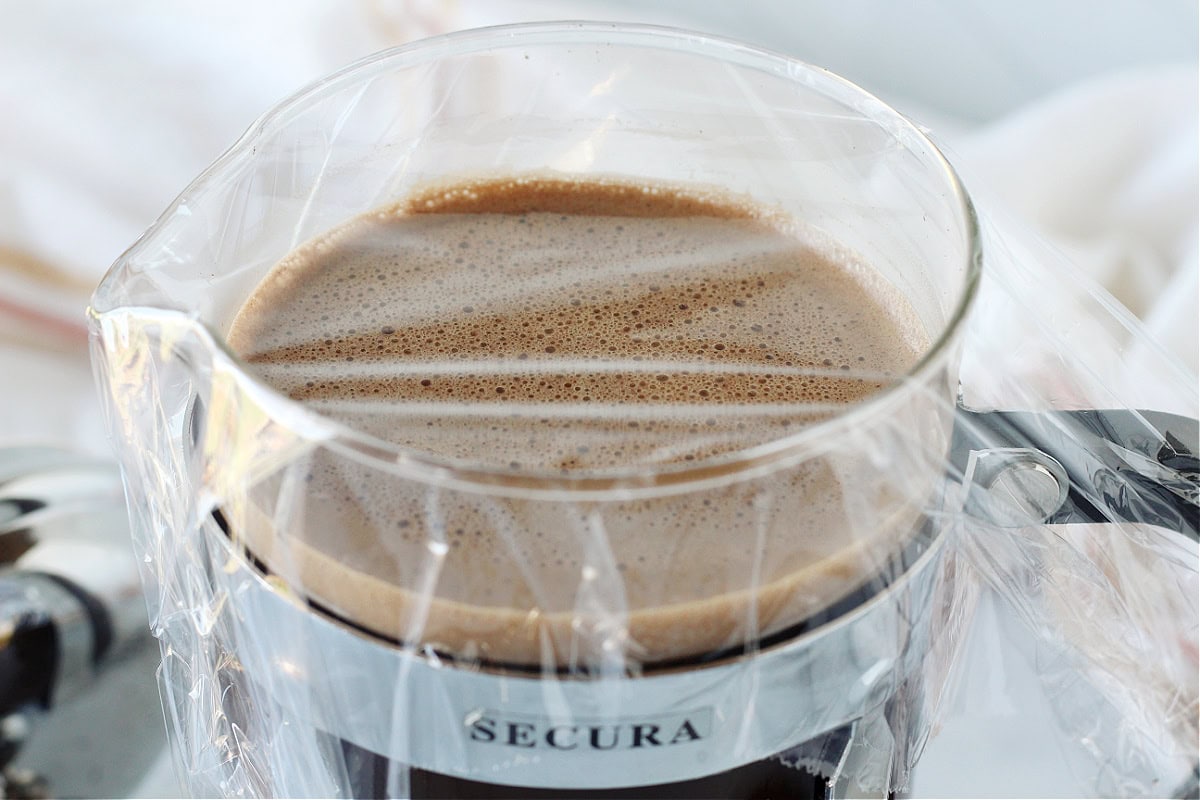 Plastic wrap over cold brew in a glass French press.
