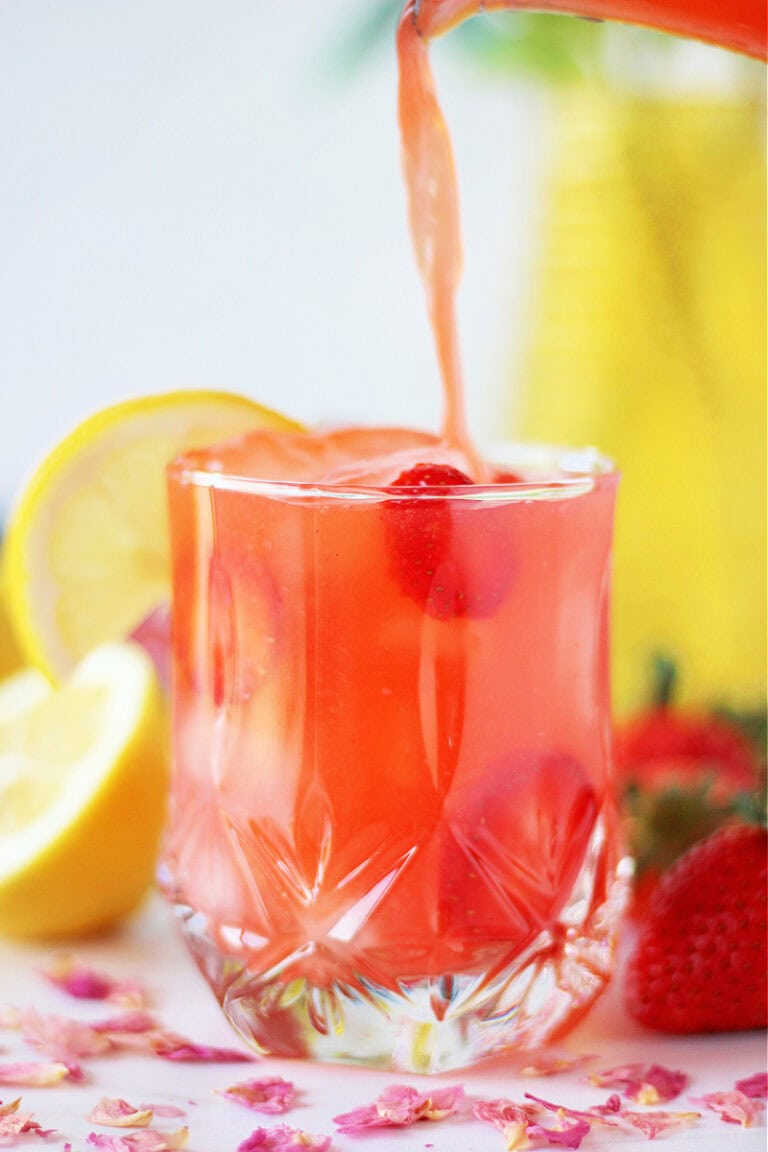 Filling a glass with homemade strawberry lemonade.