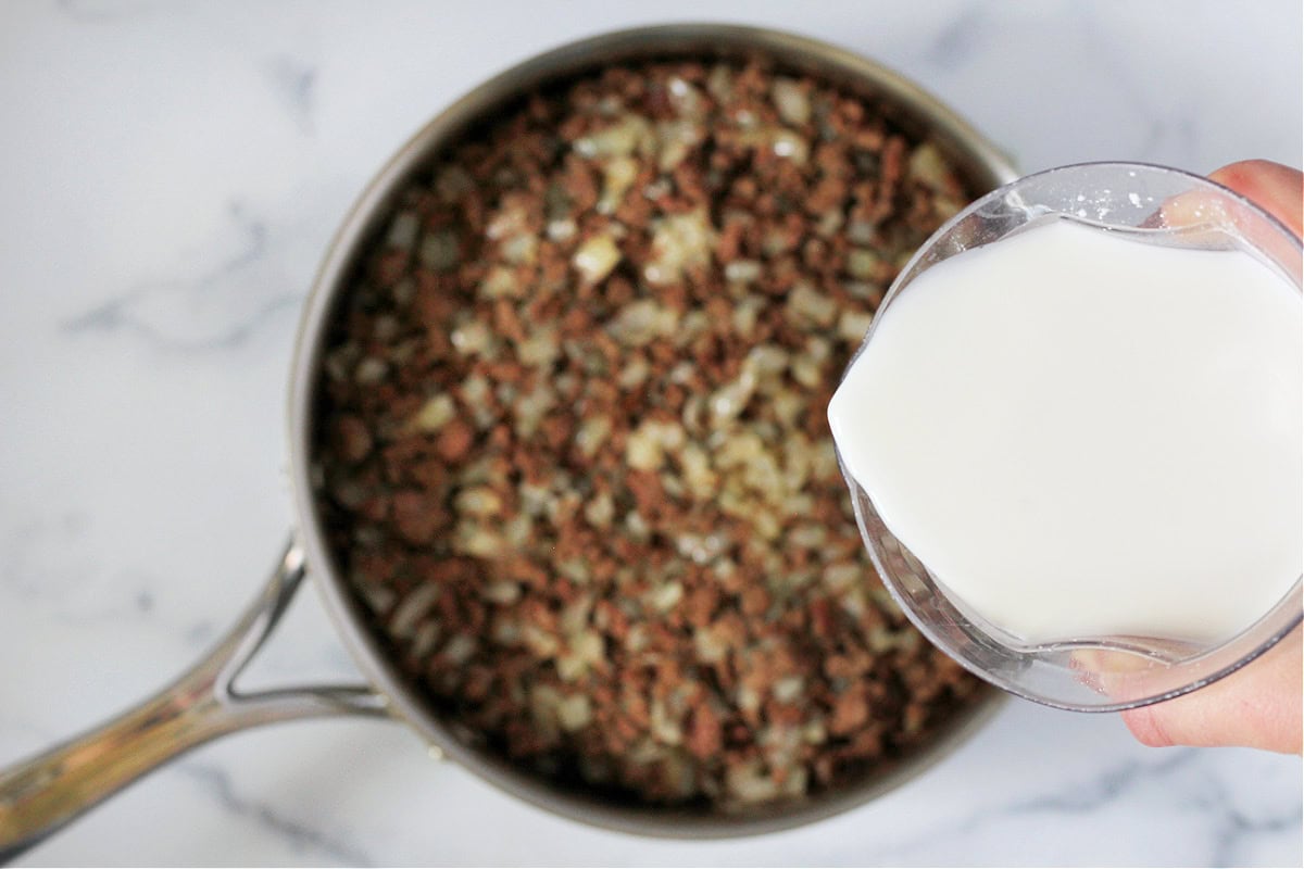 A milk cornstarch mixture poured into ground beef and onions in a sauté pan.