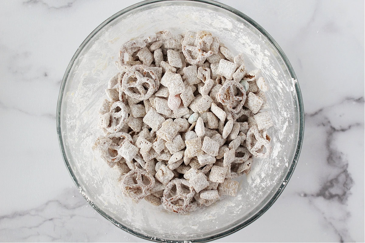Pretzels, Chex cereal, jelly beans, and M&Ms coated in powdered sugar in a bowl.