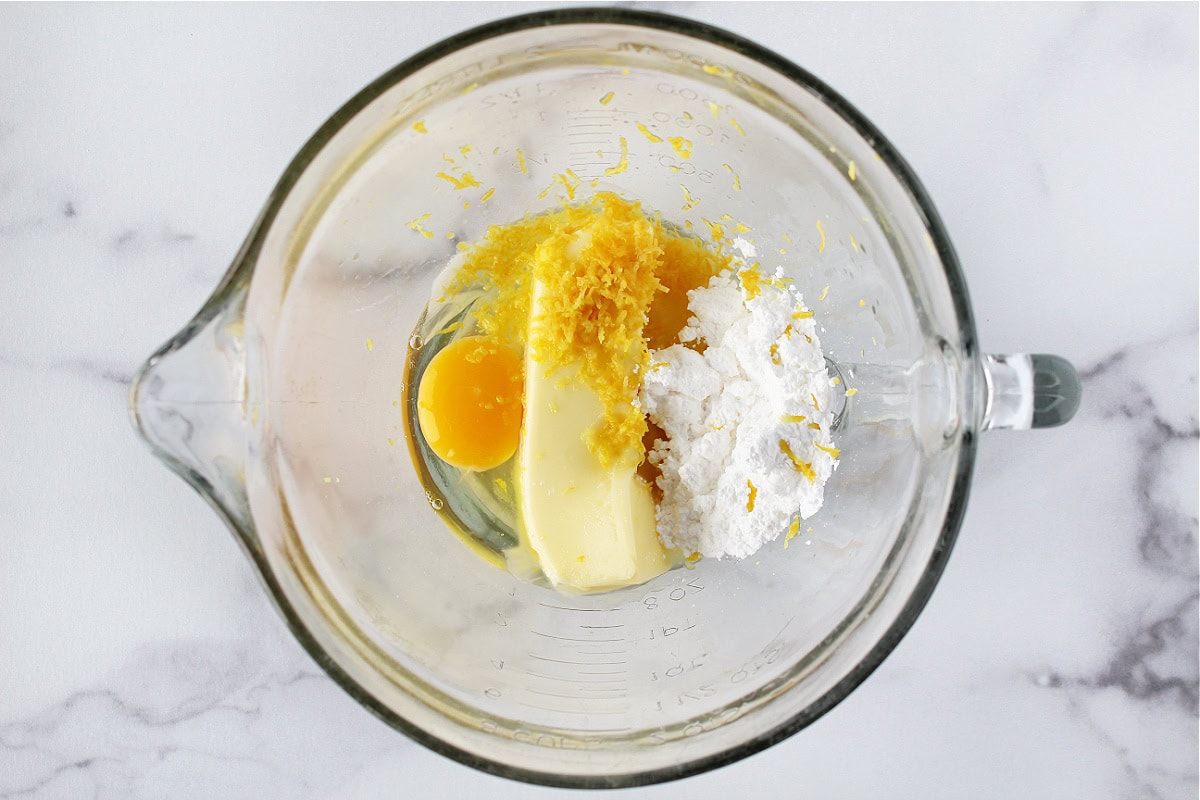 An egg, lemon zest, butter and powdered sugar in a glass mixing bowl.