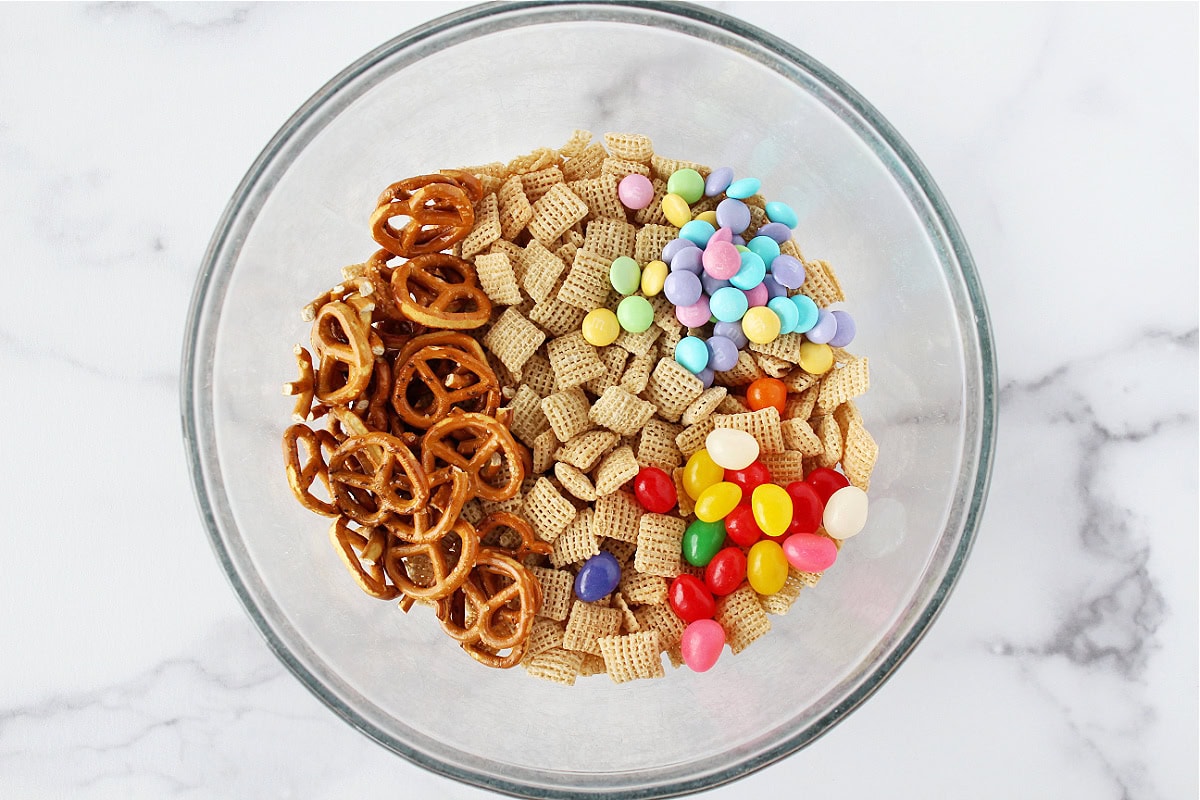Pretzels, Chex cereal, jelly beans, and pastel M&Ms in a glass bowl.